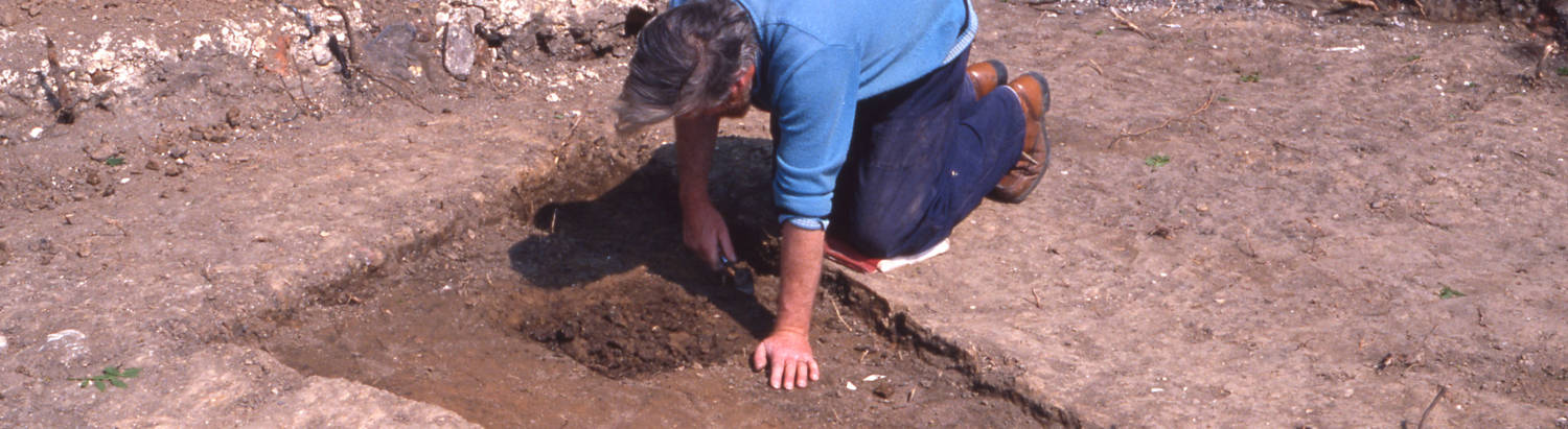 Archaeologist kneeling in trench digging with trowel